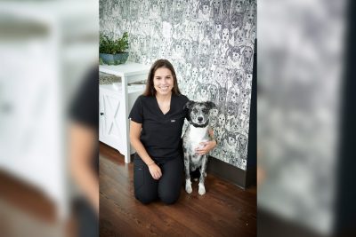 Rachael Dunn '10, DVM '14 sitting with a black and white dog while wearing black scrubs.